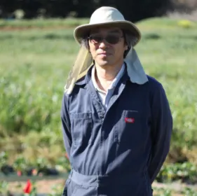 Joji, wearing a hat with ear flaps, stands in a field