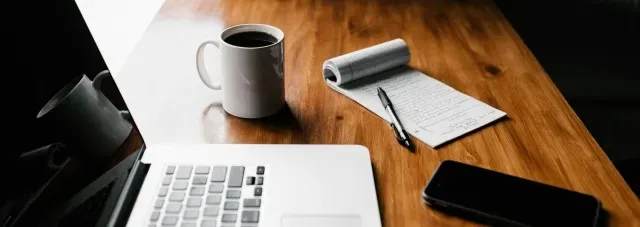 Checklist, coffee cup, and laptop on a desk.