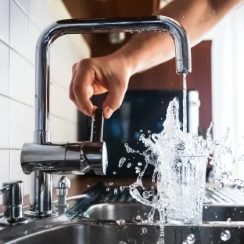 Persona abriendo llave del grifo y el agua saliendo del grifo