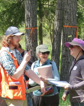 Three people standing and laughing outside. 